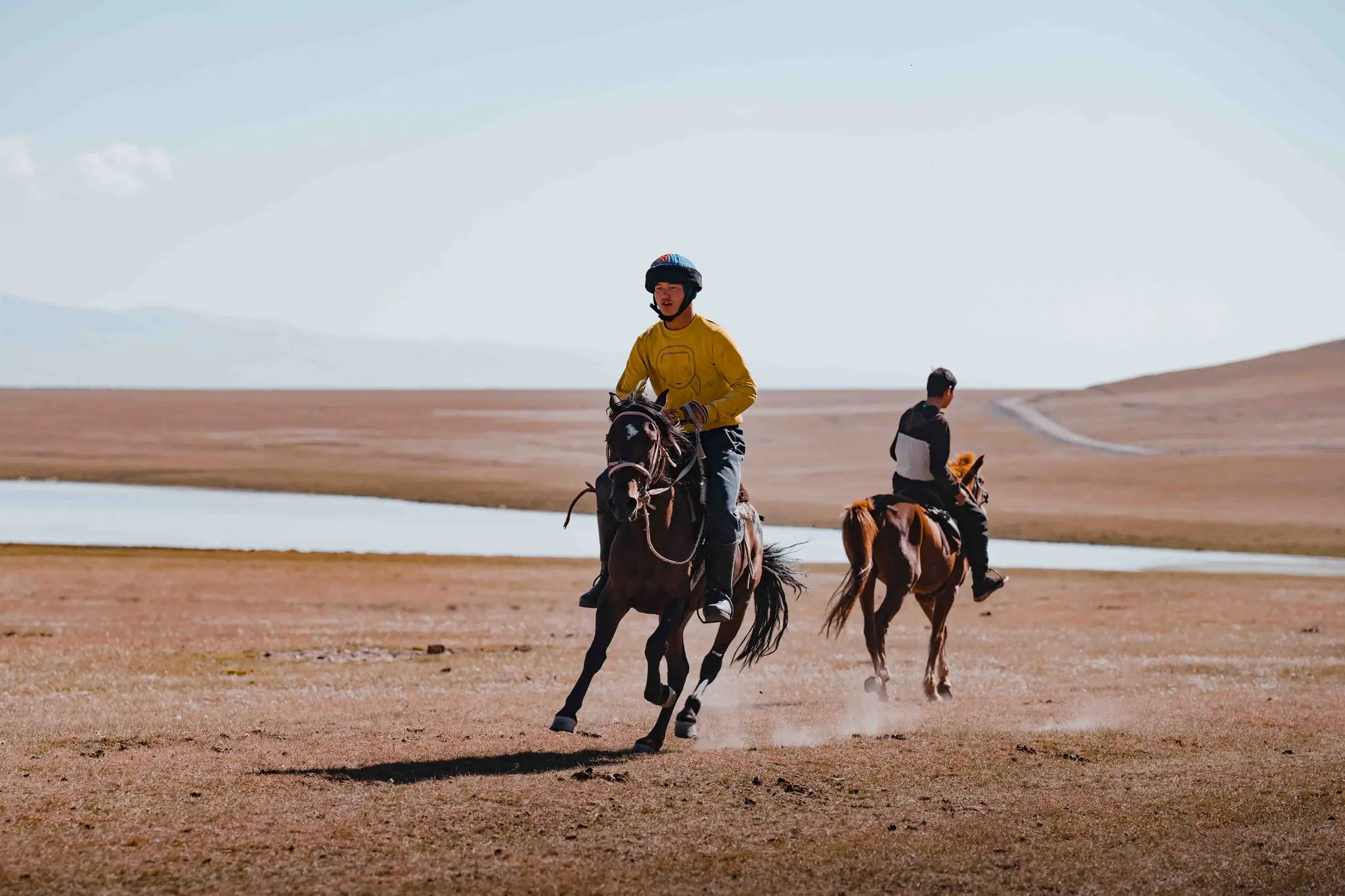 zwei Menschen, die durch eine weite, trockene Landschaft reiten