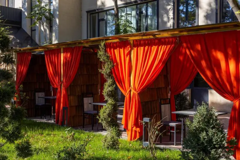 Outdoor restaurant seating with vibrant orange curtains and green lawn