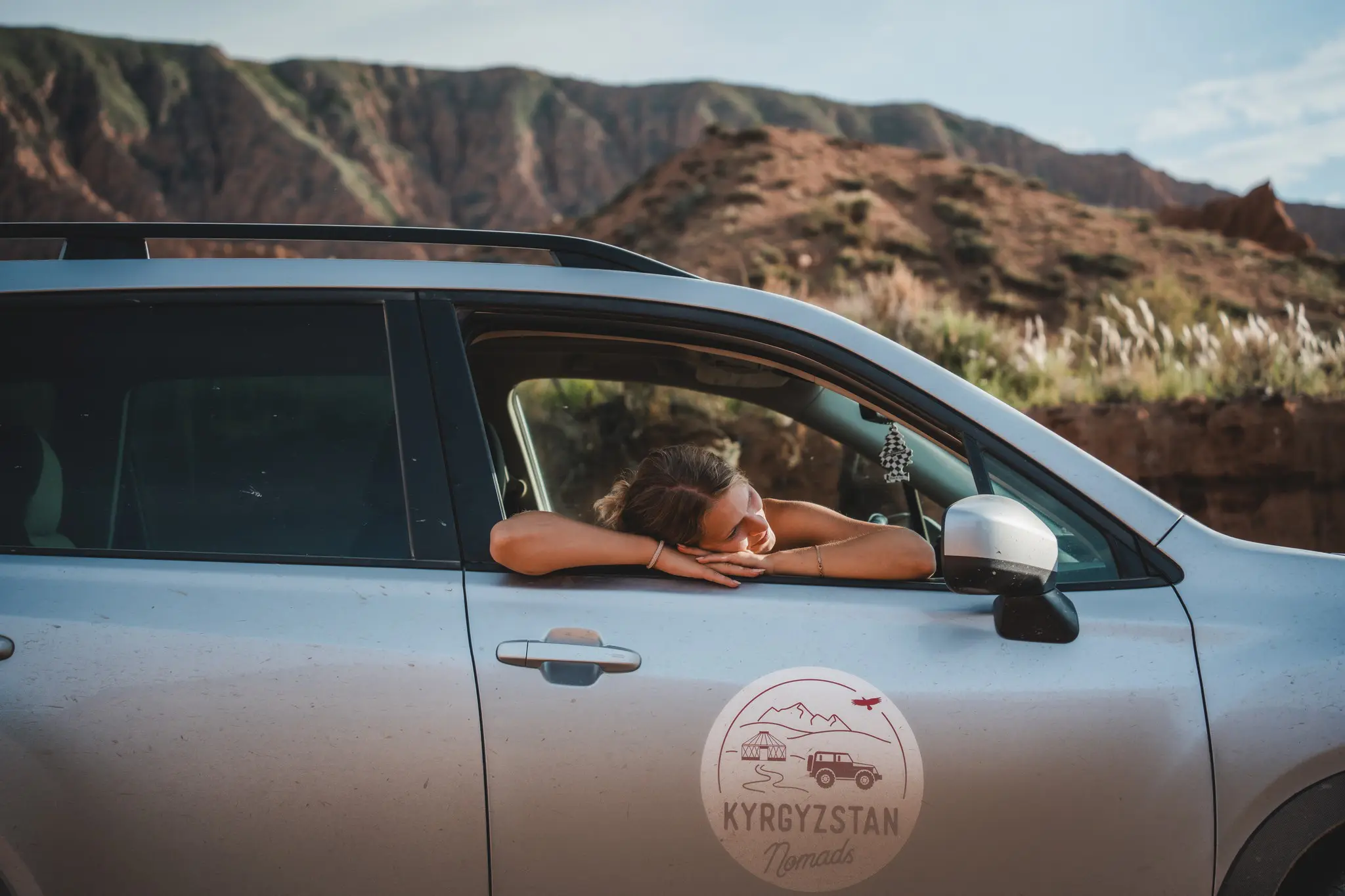 woman resting in car window with Kyrgyzstan mountains in background
