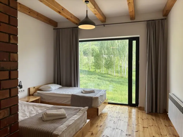 cozy twin bedroom with wooden beams and a view of green trees