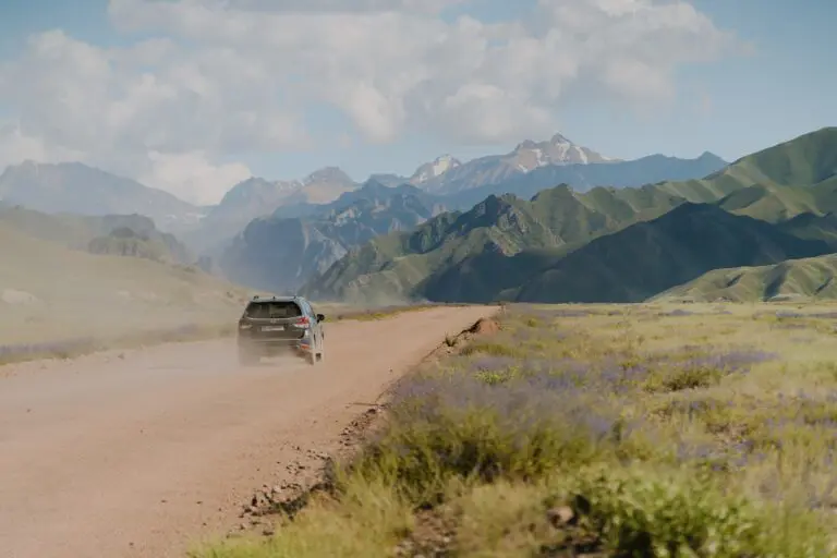 car driving on a dusty road through mountains and fields