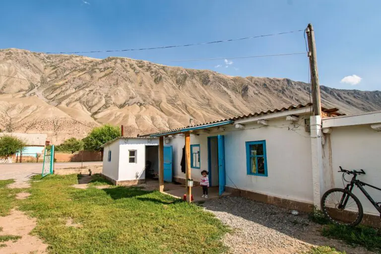 small child standing outside a white house with blue trim in Kyrgyzstan