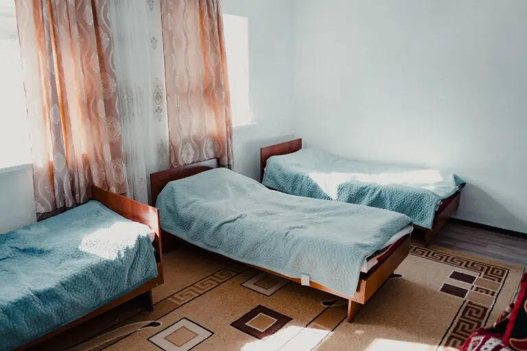 three single beds in a bright room with patterned curtains and rug