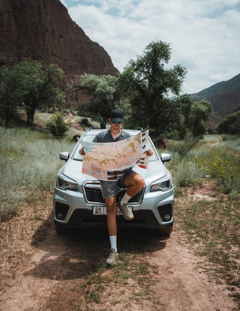 man with map leaning on car in mountainous landscape