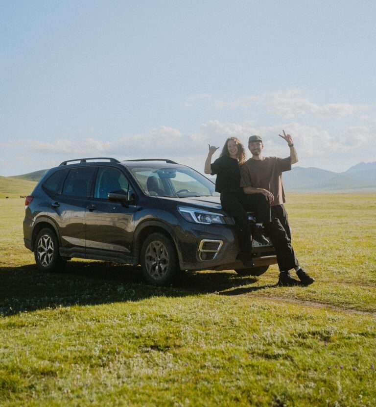 couple posing with car in vast green landscape