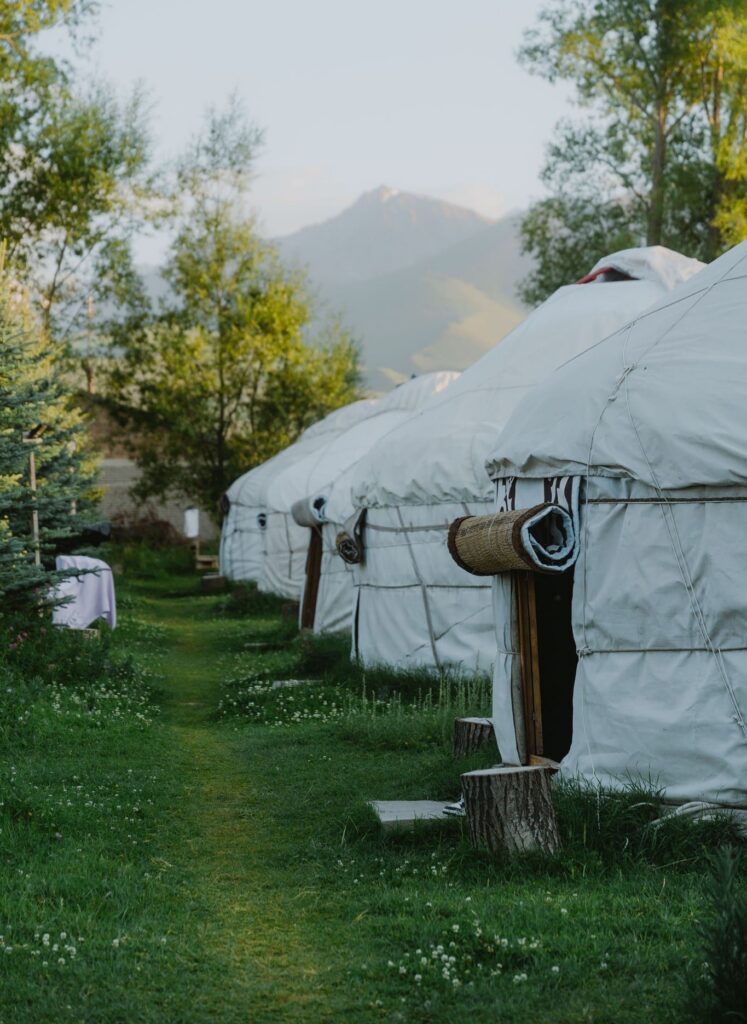 row of yurts in a green field with mountains in the background